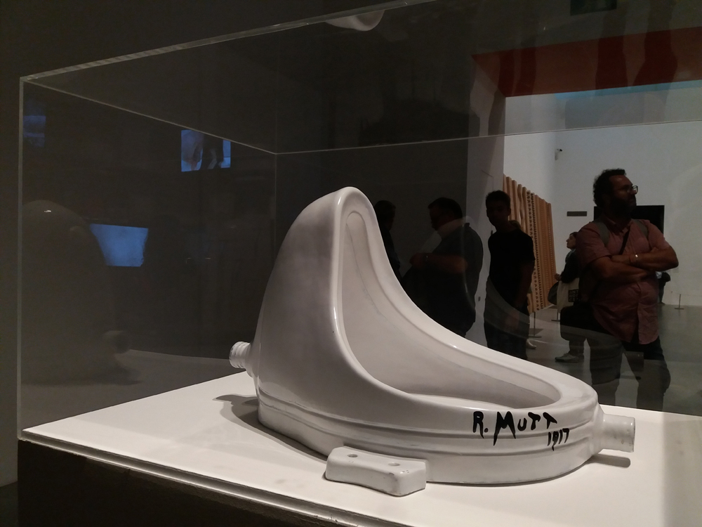 A white toilet on display in a glass case.