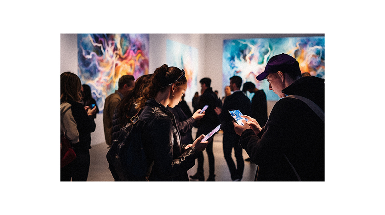 A group of people looking at their phones in an art gallery.