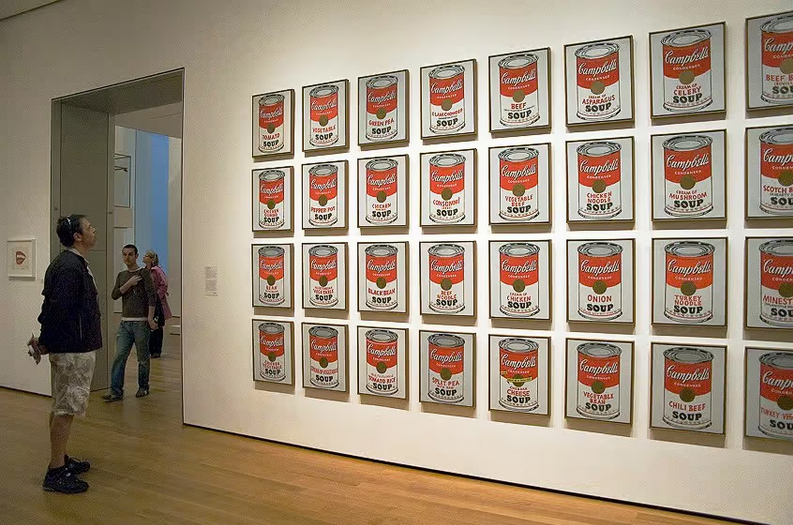 A group of people looking at a display of cans of soup.