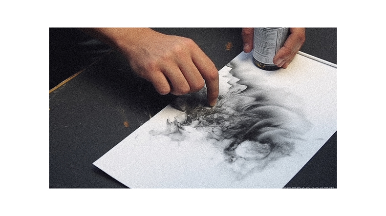 A person drawing a black and white drawing on a piece of paper.