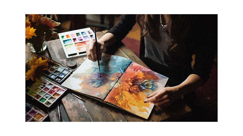 A woman is painting with watercolors on a table.